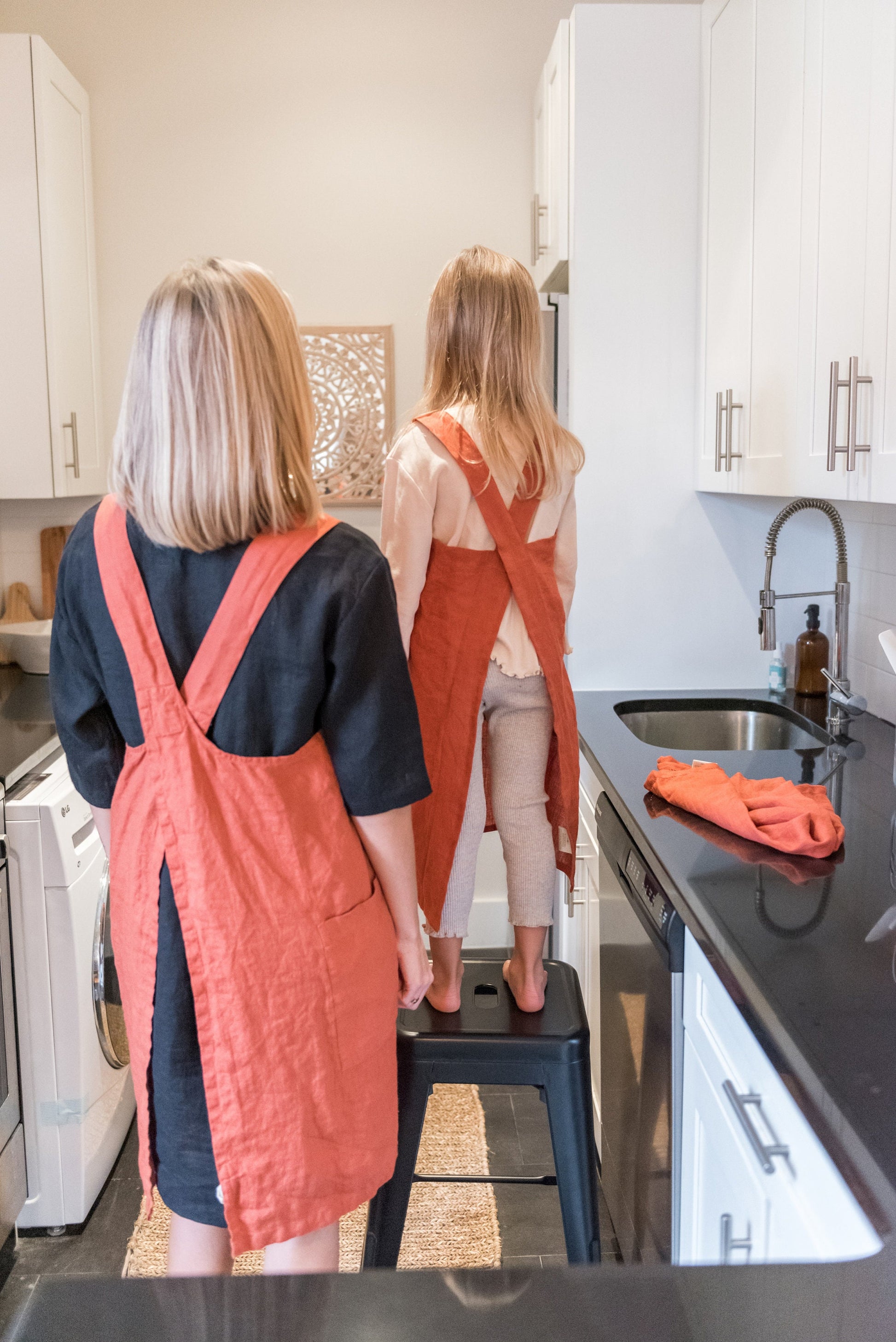 Young woman and a young girl wearing matching linen aprons - back view 